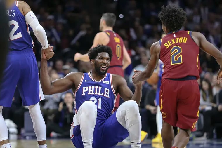 Joel Embiid getting a hand up from teammate Tobias Harris (left) and the Cavaliers' Collin Sexton during the third quarter Tuesday night.
