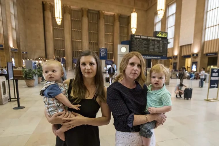 Lacey Kohlmoos (left), 34, holding 9-month-old Finn Heckert, and Samantha Matlin, 36, holding Logan Matlin, 21-month-old, in Amtrak’s 30th Street Station on Tuesday.  CLEM MURRAY / Staff Photographer