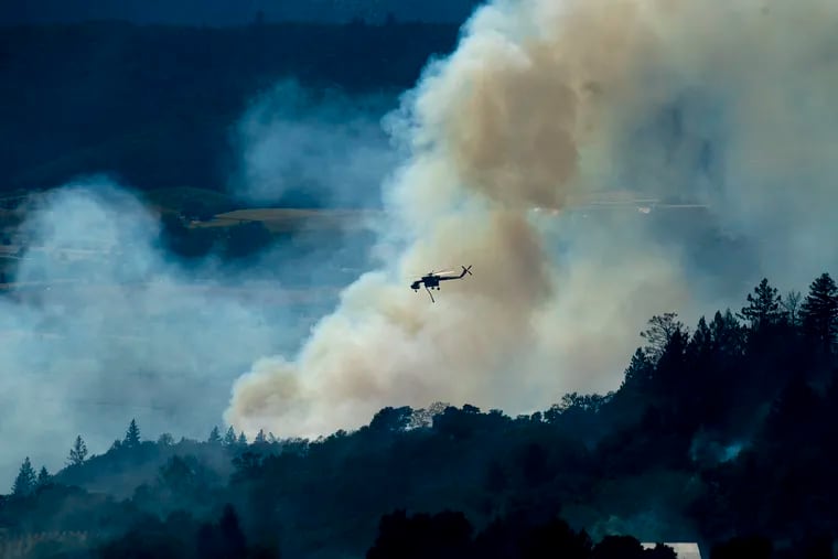 A helicopter passes a smoke plume as the Kincade Fire burns in unincorporated Sonoma County, Calif., on Thursday.