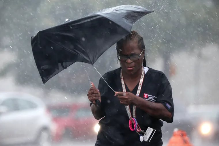A woman carries a broken umbrella during a summer downpour. Winds the next few days could claim a few umbrellas and rip sand off beaches at the Shore.