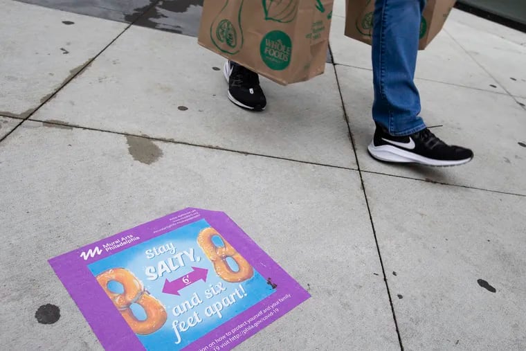 Stickers designed by Mural Arts of Philadelphia have been placed on the sidewalk along S. Broad Street  to support social distancing on April 25, 2020. Public health departments should public with local news to spread factual COVID vaccine information, write Steven Waldman and Susan Coffin.