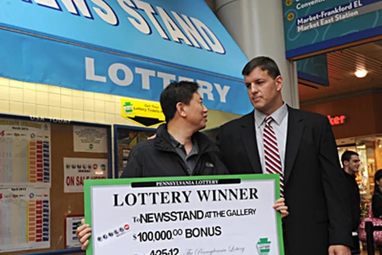 Selling a winning ticket has rewards, too. Mr. Kim (left, who withheld his first name), owner of the Newsstand at the Gallery, across from SEPTA's 12th and Market headquarters, gets a check for $100,000 from Pennsylvania Lottery executive director Todd Rucci. APRIL SAUL / Staff Photographer