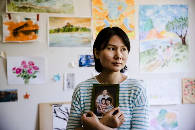 In this Wednesday, May 9, 2018 file photo, Hua Qu, the wife of  detained Chinese-American Xiyue Wang, poses for a photograph with a portrait of her family in Princeton, N.J. Iran's foreign minister says a detained Princeton graduate student will be exchanged for an Iranian scientist held by the U.S. Mohammed Javad Zarif made the announcement on Twitter on Saturday, Dec. 7, 2019. The trade involves graduate student Xiyue Wang and scientist Massoud Soleimani. Wang was sentenced to 10 years in prison in Iran for allegedly “infiltrating” the country and sending confidential material abroad. His family and Princeton strongly denied the claims.