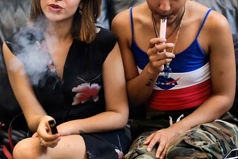 In this June 8, 2019, file photo, two women smoke cannabis vape pens at a party in Los Angeles.  Massive amounts of smoke and ash will take a toll on this year's marijuana crop. Darkened skies can also stunt the plants' growth. (AP Photo/Richard Vogel)