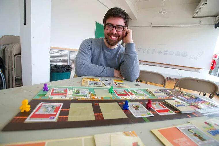 Board game designer Jason Tagmire sits behind one of his creations - "Pixel Lincoln" - at the SoHa Arts Studio in Haddon Township, where he has an office.