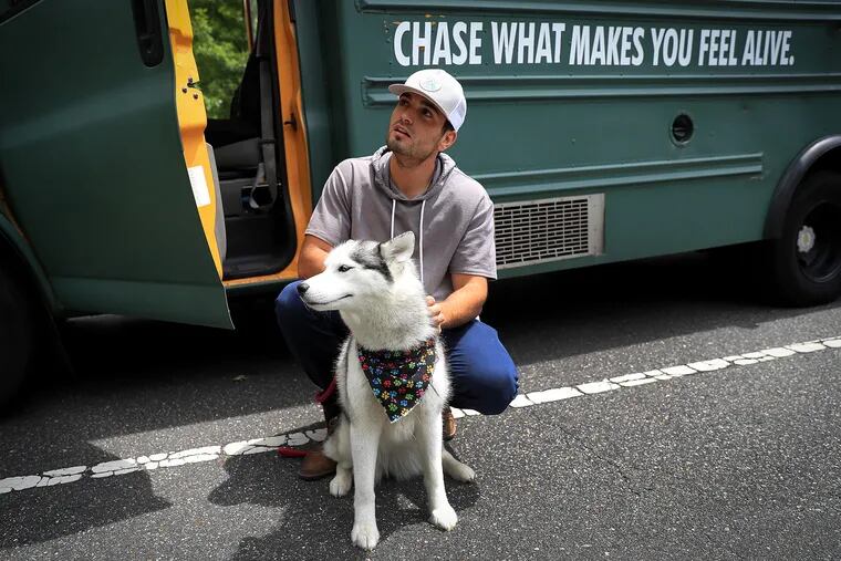Michael Burlotos pets his dog, Bailey, next to his converted school bus parked in Bellevue State Park in Wilmington, Del on June 1, 2021. Burritos as been traveling the U.S. in the bus with his dog.