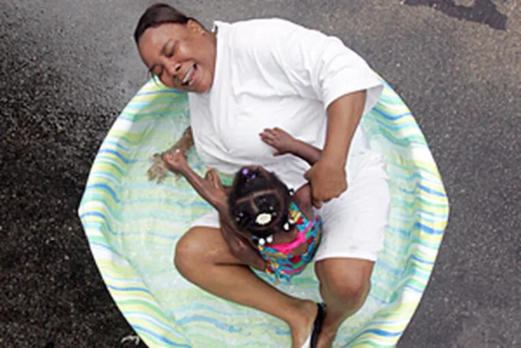 Cortez Bennett, 36, hops in a kiddie pool to cool off with one-year-old Cianni Harris, a neighbor, in the 2500 block of Bonnaffon Street in Philadelphia.