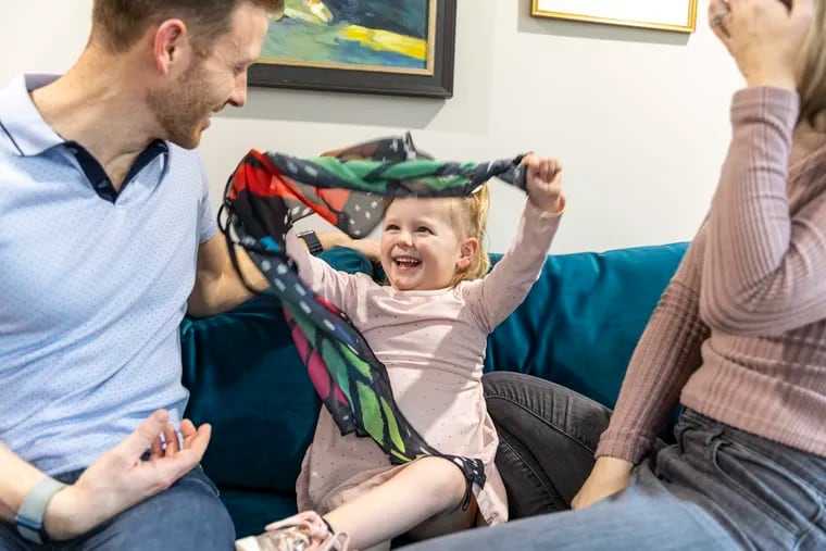 Ben Prosser and his wife, Erin, play peek-a-boo with their daughter, Lucy, 4, at their home in Swarthmore. Lucy was born with a rare neurological disorder that her father, a Penn scientist, has now devoted his life to studying.