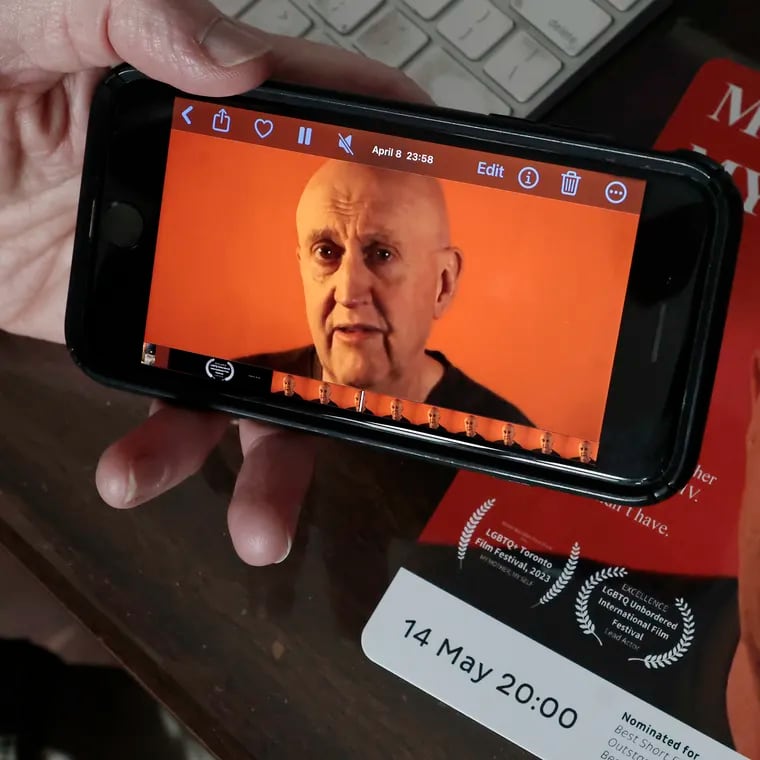 Filmmaker Lary Campbell plays his short film on his phone. The movie card is in the background. Lary was photographed in his Magnolia, N.J. home on Friday, May 3, 2024. Campbell directed and performed the short film, My Mother, My Self. It is the story of the day he told his mother he had HIV. Now the film is being shown at an international film festival in France.