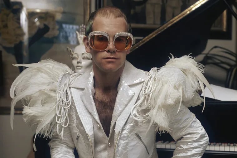 English pop singer Elton John in a flamboyant stage outfit of white suit with feather trim and rhinestone encrusted glasses, circa 1973.