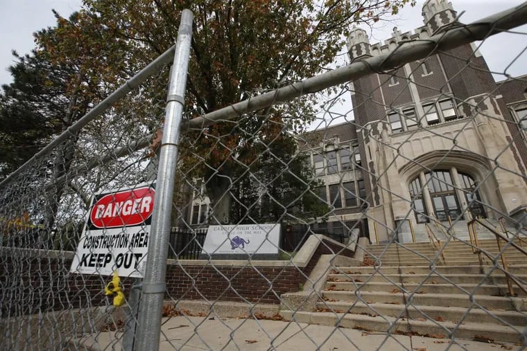 Construction fencing and a caution sign block the front entrance to the shuttered Camden High School building.