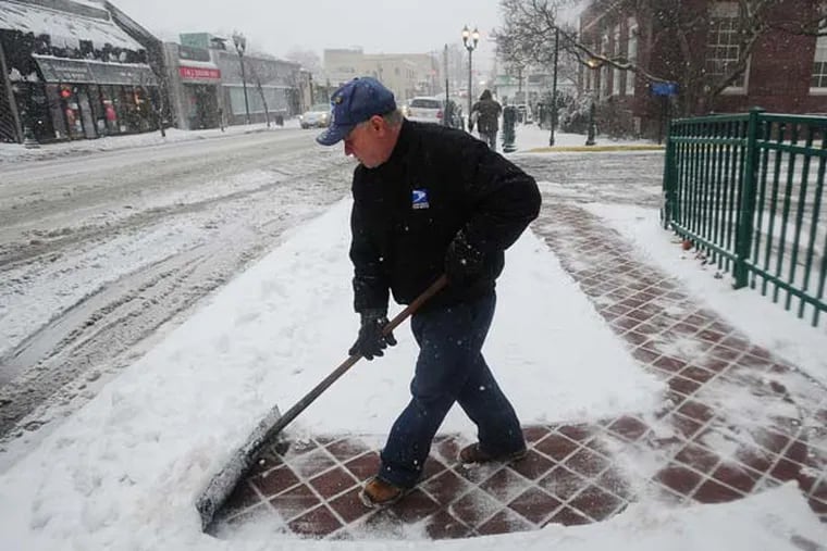 USPS worker Jiuseppe Gramuglia cleans snow, not far from the post office on Main Street in Fort Lee, N.J. as a winter storm hits the region on Friday, Feb. 8, 2013. (AP Photo/The Record of Bergen County, Marko Georgiev)