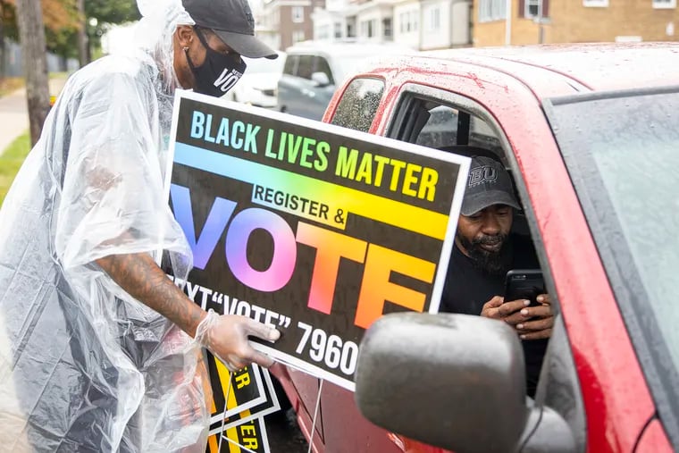 Damien Grobes, 42, of West Philadelphia, lead manager for One Pennsylvania, helps a man driving by to text their number and hands them a sign to help others register to vote in North Philadelphia, on Sept. 26.