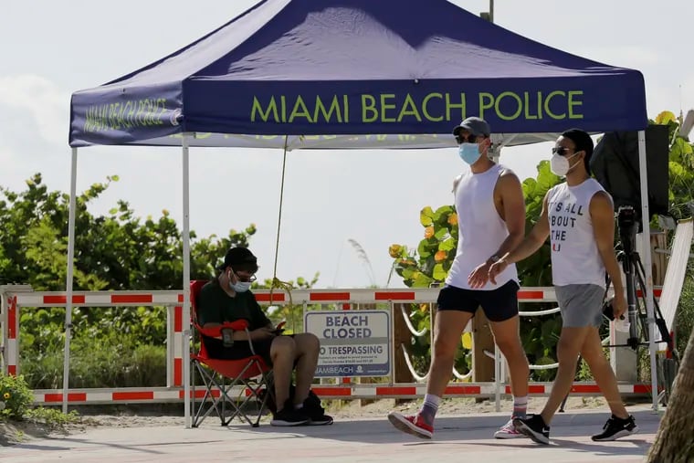 People wearing protective face masks walk past a closed entrance to the beach during the new coronavirus pandemic, Friday, July 3, 2020, in the South Beach neighborhood of Miami Beach, Fla. Beaches throughout South Florida are closed for the busy Fourth of July weekend to avoid further spread of the new coronavirus.
