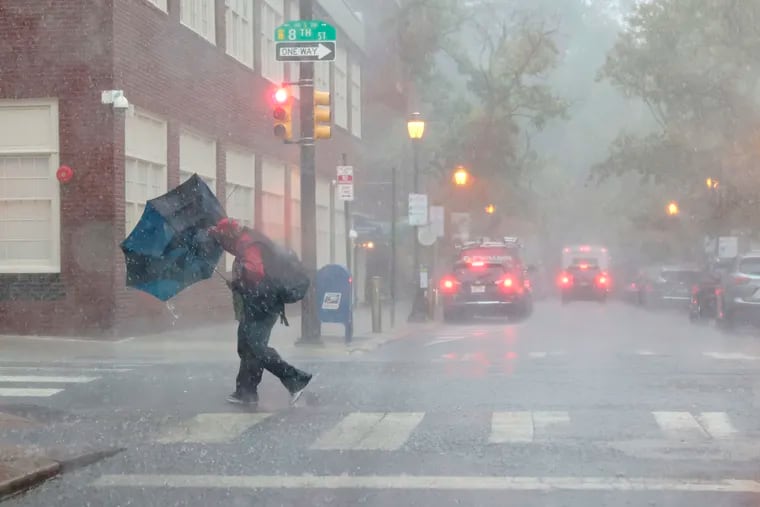 A man struggles to keep his grip as the powerful winds and rain invert his umbrella as he crosses 8th and Locust Streets last month. Strong storms are expected Saturday.