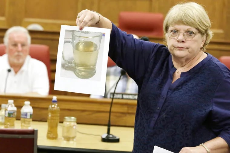 Anne Flynn shows the council a photo of a glass of brown Maple Shade water. She fears the tainted water may have caused her cancer. Officials blamed the color on old iron pipes, and said there was no health issue.