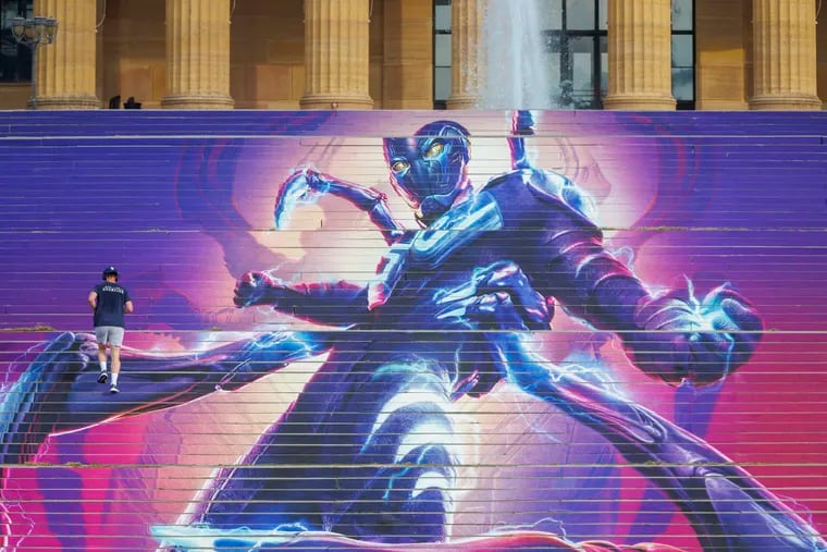 A runner heads up the steps of the Philadelphia Museum of Art, which are covered with a temporary vinyl poster for the new DC Comics superhero movie, "Blue Beetle," which premieres Friday.