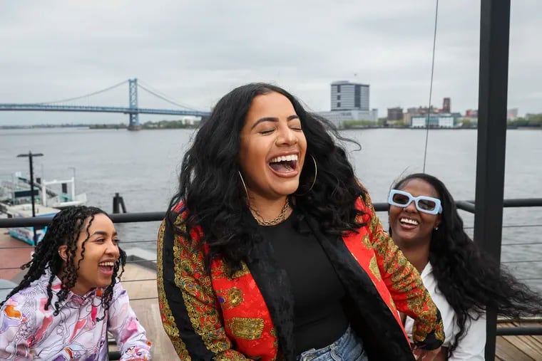 Delilah Dee (center), founder of Jefatona, DJ Flakka (left), and DJ Bria G (right), laugh while posing together for a photo on the rooftop of Liberty Point in Philadelphia on Thursday, April 18, 2024. Jefatona, Philly's reggaeton and Caribbean party created to be a safe space for women, will have their own exclusive space at El Movimiento's Cinco de Mayo Festival on the waterfront this weekend.