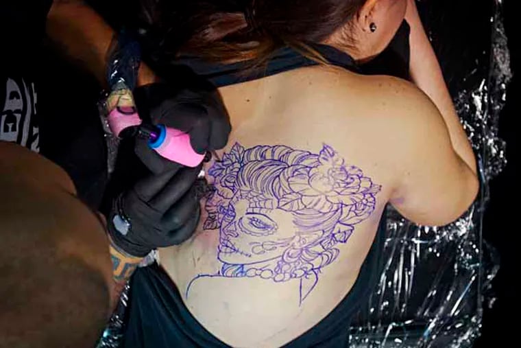 Christina Benavides gets a Catrina Day of the Dead tattoo designed by Oscar " The Bear" at the 16th annual Philadelphia Tattoo Convention at the Convention Center. ( RON TARVER / Staff Photographer ) February 2, 2014