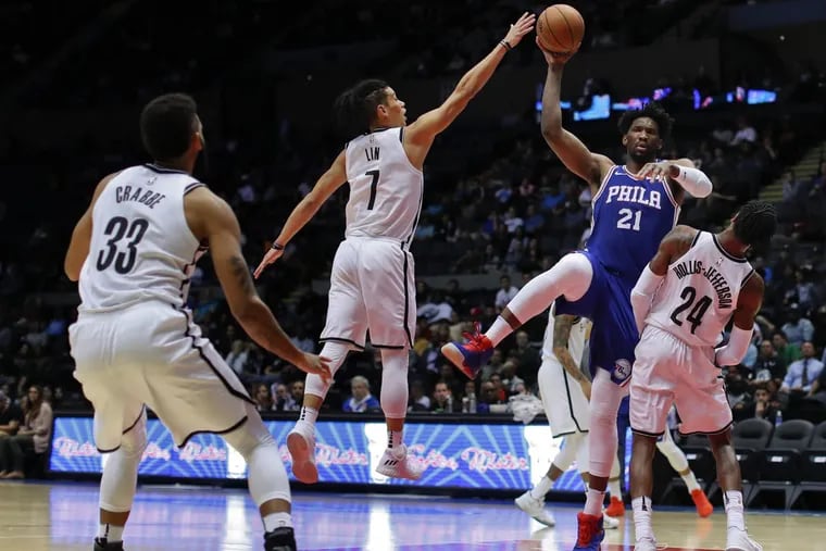Sixers center Joel Embiid passes the ball over Nets guard Jeremy Lin (center) and forward Rondae Hollis-Jefferson (right). Embiid had 22 points in his preseason debut.