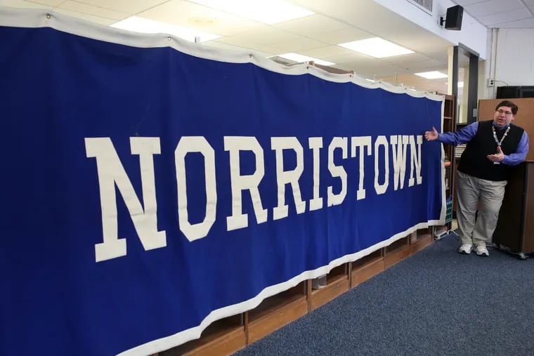 Robert (B.J.) Schmalbach, high school librarian and 95' alumni  shows off Norristown banner in the library at Norristown Area High School.