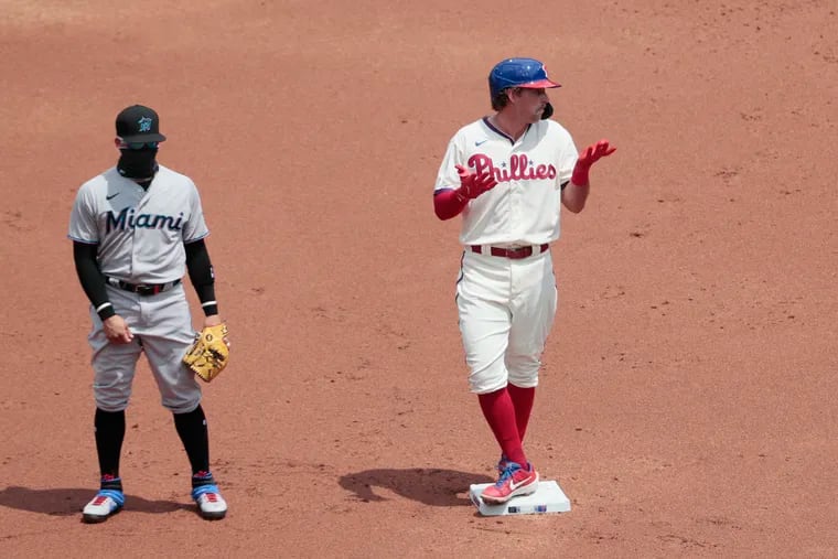 With an unidentified Marlins players looking on, the Phillies' Rhys Hoskins gestures to the dugout Sunday. Sixteen Marlins players have tested positive for COVID-19 since last Friday.