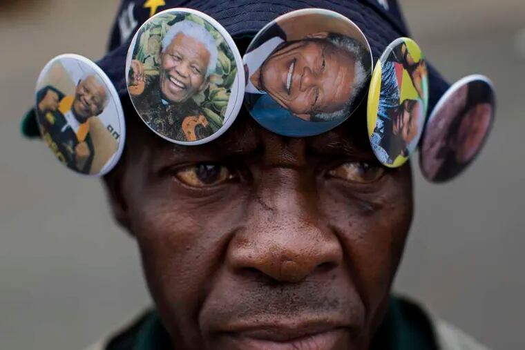 Mac Arthur Mti wears badges for sale with the familiar smiling image of the late President Nelson Mandela in Soweto Township near Johannesburg, South Africa. Below, lasers beam an image of Mandela, known popularly by his clan name, Madiba, onto Cape Town's Table Mountain.