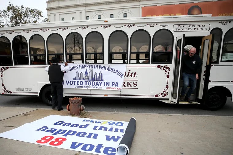 Trolley operator Shaun Baldie (left) and Michael Barnes (right), president and business manager of the local IATSE stagehands union, hang a sign as they prepare the "Voter Express" trolley outside The Met in North Philadelphia on Sunday.