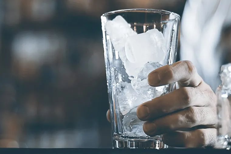 Glass with ice cubes on the background of the bar in barman hand.