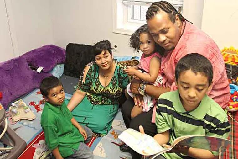 A program nicknamed "Baby College" has come to Camden through the Promise Neighborhood Family Success Center. It aims to help parents do a better job -- and ease the child developmental effect of what's now being recognized as a public health issue: poverty.  In the the "Book NooK"/computer center, Daghee Shakes, 7, right, reads a book as L-R: his brother Rajeev, his mother Sherri Shakes, sister Maexing, and father Darnell Shakes look on. ( CHARLES FOX / Staff Photographer )