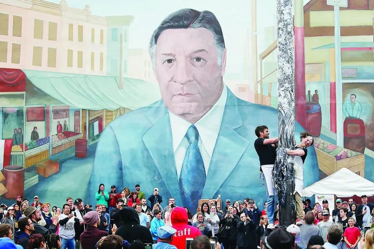 Participants try to climb the greased pole with the mural of former Philadelphia Mayor Frank Rizzo looking on at the South 9th Street Italian Market Festival on Saturday, May 21, 2016.