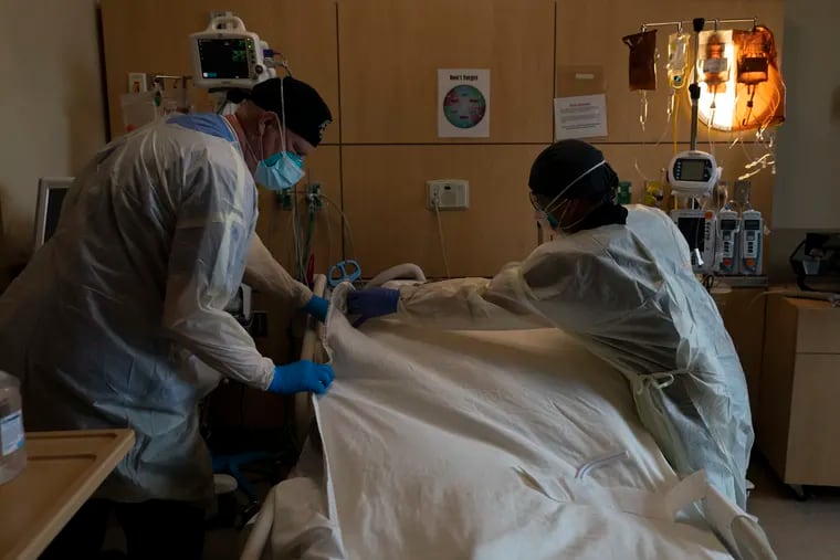 Respiratory therapist Frans Oudenaar, left, and registered nurse Bryan Hofilena cover a body of a COVID-19 patient with a sheet at Providence Holy Cross Medical Center in Los Angeles.