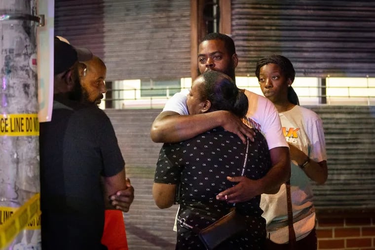 Sircarr Johnson Sr., center, is comforted by family outside of his son's clothing store, Premiére Bande, on 60th Street near Walnut in West Philadelphia. Johnson's son, Sircarr Johnson Jr., 23, was killed in a triple shooting at a July 4th cookout he had at his store Sunday night. A 22-year-old man, whose identity has not been released, was also killed, and a 16-year-old girl was injured by the gunfire.