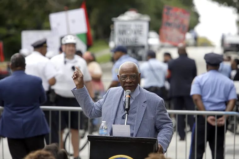 Former Mayor W. Wilson Goode Sr. speaks to supporters, as protesters demonstrate in the background, during a ceremony to celebrate the naming of a street after him Friday Sept. 21, 2018. Goode said he was responsible for dropping a bomb on a home full of people 33 years ago, but said he would not be defined by one day of his life