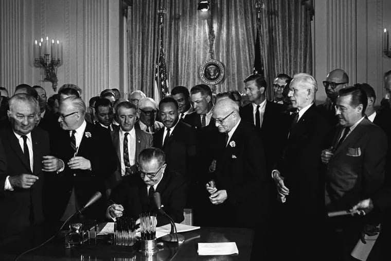 President Lyndon B. Johnson signing the 1964 Civil Rights Act as Martin Luther King Jr. and others look on.
