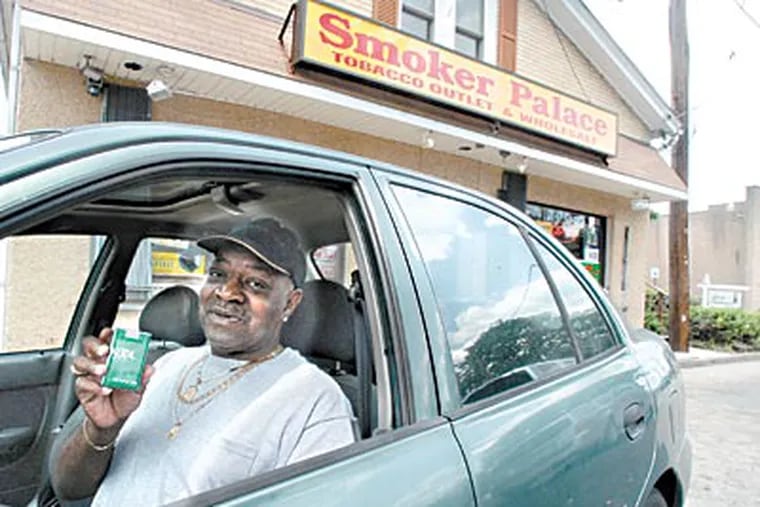 Milton Glover of Trenton shows cigarettes he bought at Smoker Palace in Morrisville, where prices lure drivers across the “Trenton Makes” span. (April Saul / Staff Photographer)