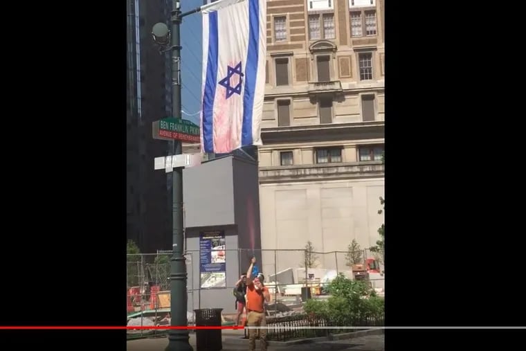 Police are trying to identify the suspect shown in a video spraying a red substance onto the Israeli flag that flies over the Benjamin Franklin Parkway.