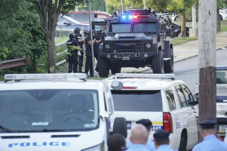 Philadelphia Police SWAT unit officers behind an armored vehicle with weapons drawn during a standoff.