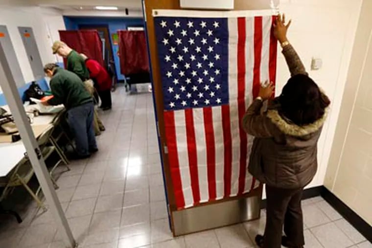 FILE PHOTO: Evelyn Dennis, of Fort Lee, N.J., hangs a U.S. flag as election workers set up voting booths at Memorial Elementary School in Little Ferry, N.J., on Election Day, Tuesday, Nov. 6, 2012. (AP Photo/Julio Cortez)