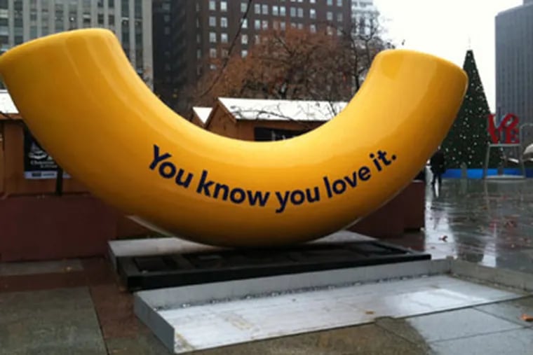 A giant yellow macaroni bearing a message from Kraft was installed in Love Park on Nov. 22, 2011. In the background are the shops of this year's Christmas Village, the Love sculpture and the city's holiday tree, which will be lit Dec. 7.