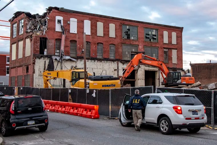 A worker from L&I is at the site in Kensington late Thursday where a 100-year-old hosiery mill was being demolished. The teardown was halted by city officials after neighbors posted a video on Wednesday showing debris tumbling from the building into the street.