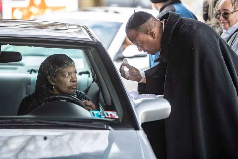 The Very Reverend Martini Shaw, right, administers the communion wafer to a St Thomas parishioner, left, as she drives through a covered area of the church to receive Holy Communion on March 15, 2020.