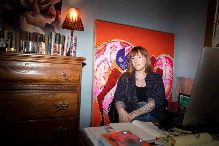 Kelsey McKinney, host of the popular podcast “Normal Gossip,” in her home office in Queen Village. Behind her is a painting by Gelbell, self-taught Australian artists who paint at the same time and epitomize McKinney's approach to creative work.