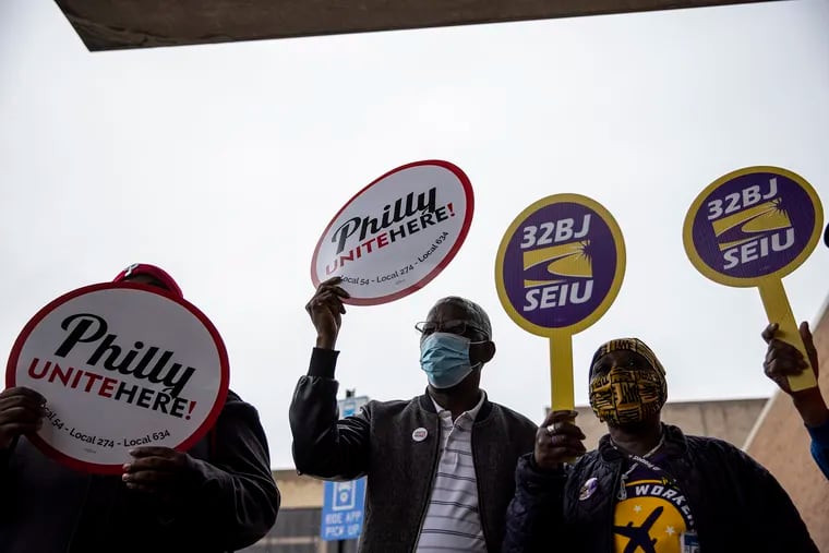 Nathaniel Sokan (center) holds a Philly Unite Here union sign before a rally earlier this month in favor of boosting wages and health benefits for workers at Philadelphia International Airport.