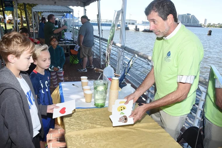 Ed Cohen of Sustainable South Jersey (right) does magic tricks with brothers Thomas (left) and Matthew Bohnyak. Cohen is manning the organization's table at the Delaware River Festival in Camden.