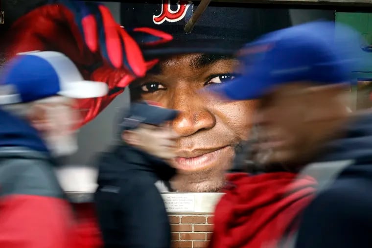 Fans walk past a photograph of former Boston Red Sox David Ortiz before a baseball game against the Toronto Blue Jays at Fenway Park in Boston.