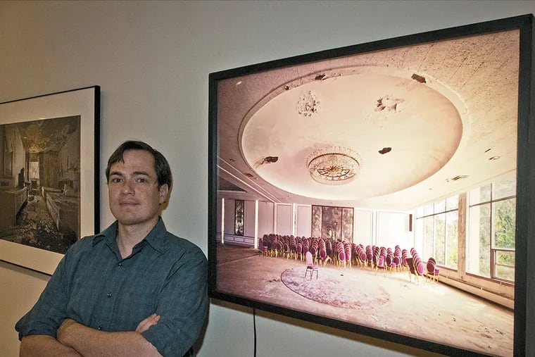Matthew Christopher stands next to one of his photographs of abandoned buildings in an exhibition called "The Age of Consequences" at the Gershman Y, 401 S. Braod Street. ( RON TARVER / Staff Photographer )
