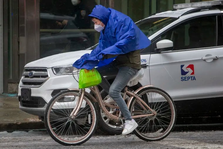 A cyclist in a plastic poncho bikes on North 13th Street in Center City on a cold windy morning last month. We're getting an encore this weekend.