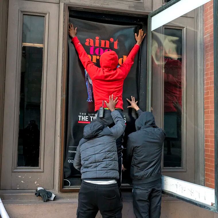 December 4, 2023: Kimmel Cultural Campus employees Tyshawn Burrell and Gary Stanford (right) help coworker Zaphier Johnson (top) put up a new marquee poster outside the Academy of Music.