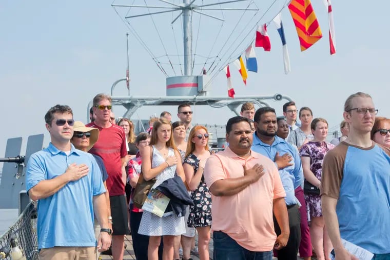 Friends and family of citizenship candidates stand for the national anthem during a naturalization ceremony aboard the Battleship New Jersey in Camden, NJ on July 4, 2018.